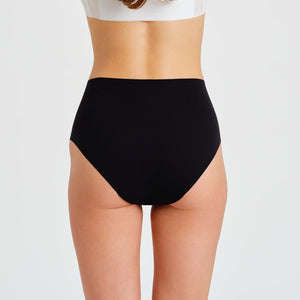 Modell trägt ooia everyday Highwaist Seamless in Schwarz – nahtlose Unterwäsche mit hohem Bund, die Slipeinlagen ersetzt. Rückansicht.