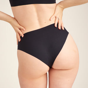 Modell trägt ooia everyday Slip Seamless in Schwarz – nahtlose Unterwäsche, die Slipeinlagen ersetzt. Rückansicht.