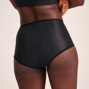 Modell trägt ooia Highwaist Extra Strong in Schwarz – Periodenunterwäsche mit hohem Bund und Glanzdetail. Rückansicht.