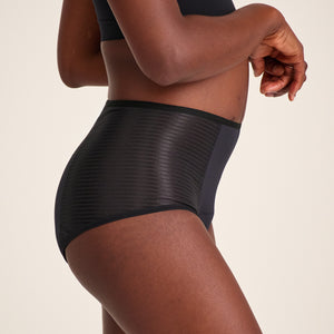 Modell trägt ooia Highwaist Extra Strong in Schwarz – Periodenunterwäsche mit hohem Bund und Glanzdetail.