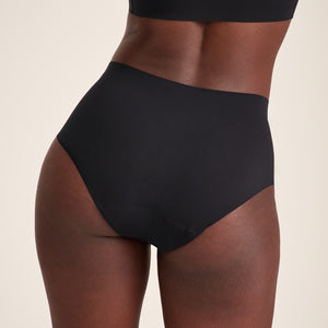 Modell trägt ooia Highwaist Seamless in Schwarz – nahtlose Periodenunterwäsche mit hohem Bund. Rückansicht.