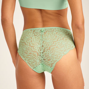 Modell trägt ooia Hipster Allover Lace in Bright Sage – Periodenslip mit durchgehender floraler Spitze. Rückansicht.