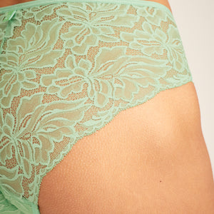 Modell trägt ooia Hipster Allover Lace in Bright Sage – Periodenslip mit durchgehender floraler Spitze. Detailansicht.