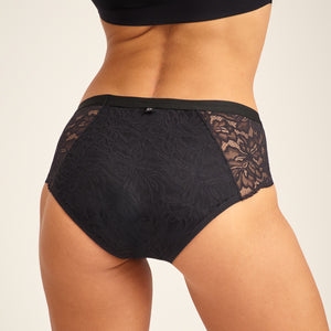 Modell trägt ooia Hipster Allover Lace Extra Strong in Schwarz - Periodenunterwäsche mit durchgehender Spitze und starker Saugstärke. Rückansicht.