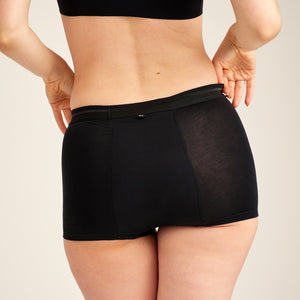 Modell trägt ooia Shorty Extra Strong in Schwarz – Periodenunterwäsche mit breitem Bund und starker Saugstärke. Rückansicht.