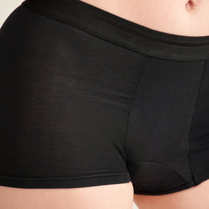 Modell trägt ooia Shorty Extra Strong in Schwarz – Periodenunterwäsche mit breitem Bund und starker Saugstärke.