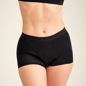 Modell trägt ooia Shorty Extra Strong in Schwarz – Periodenunterwäsche mit breitem Bund und starker Saugstärke.