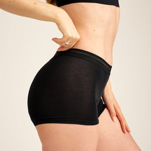 Modell trägt ooia Shorty Extra Strong in Schwarz – Periodenunterwäsche mit breitem Bund und starker Saugstärke.