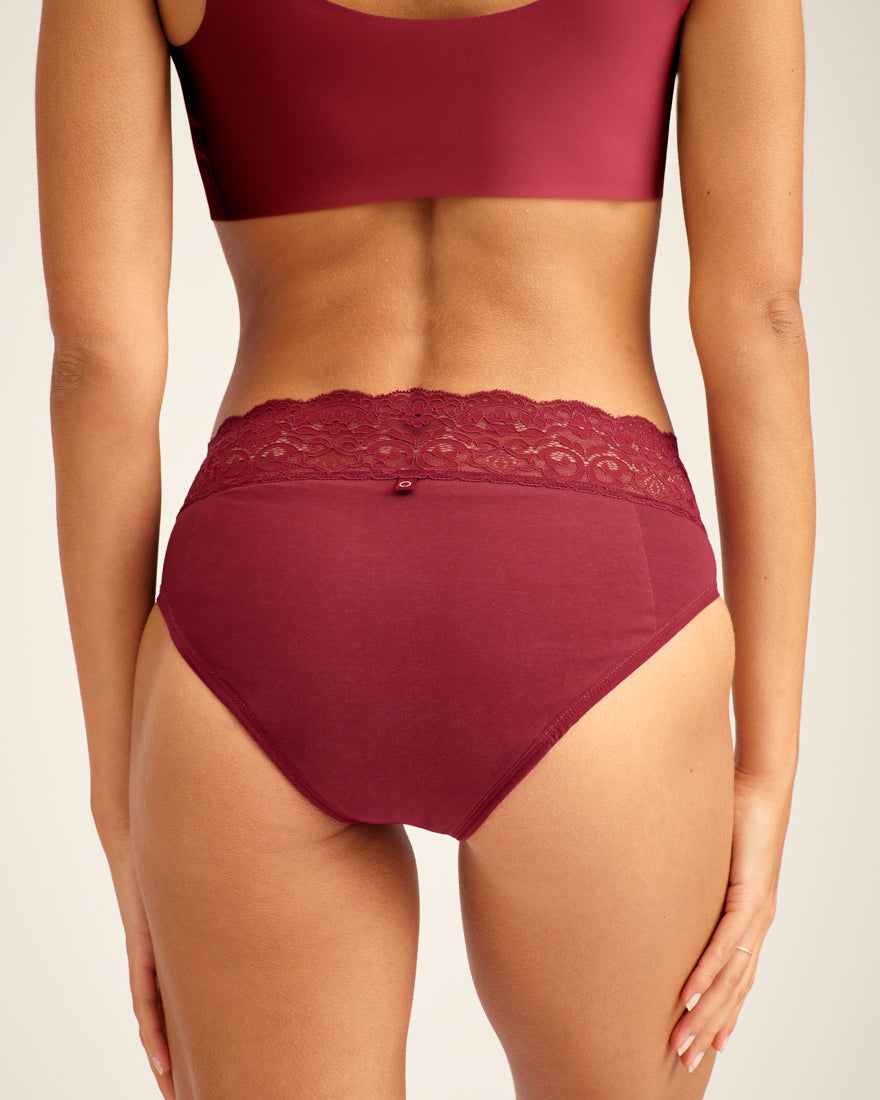 Modell trägt ooia Periodenunterwäsche Slip in Merlot, mit breiter Spitze am Bund. Rückansicht.