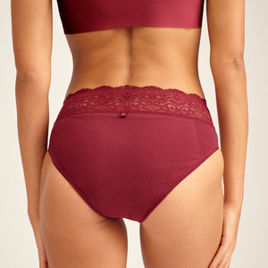 Modell trägt ooia Periodenunterwäsche Slip in Merlot, mit breiter Spitze am Bund. Rückansicht.