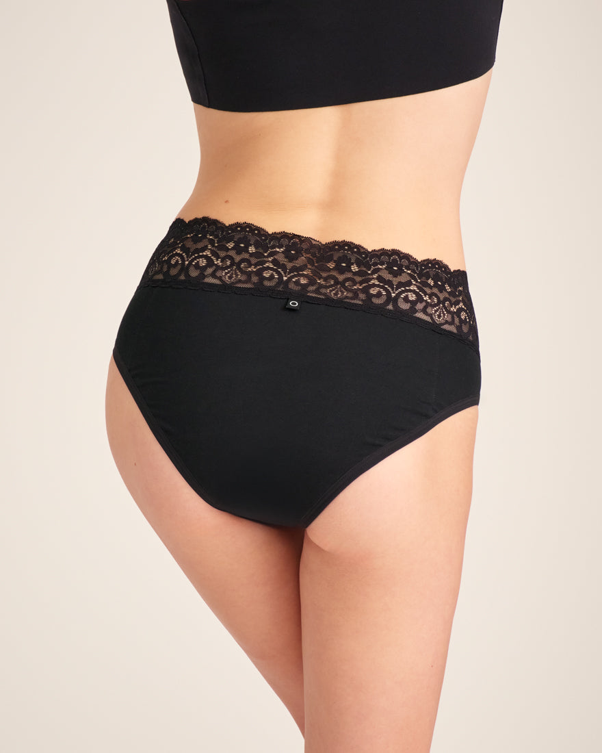 Modell trägt ooia Slip in Schwarz – Periodenslip mit breitem Spitzenbund im klassischen Schnitt. Rückansicht.