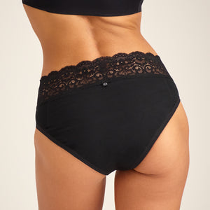 Modell trägt ooia Slip Extra Strong in Schwarz – Periodenunterwäsche mit breitem Spitzenbund im klassischen Schnitt. Rückansicht.