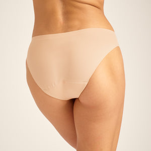 Modell trägt ooia Slip Seamless in Beige – nahtlose Periodenunterwäsche im klassischen Schnitt. Rückansicht.