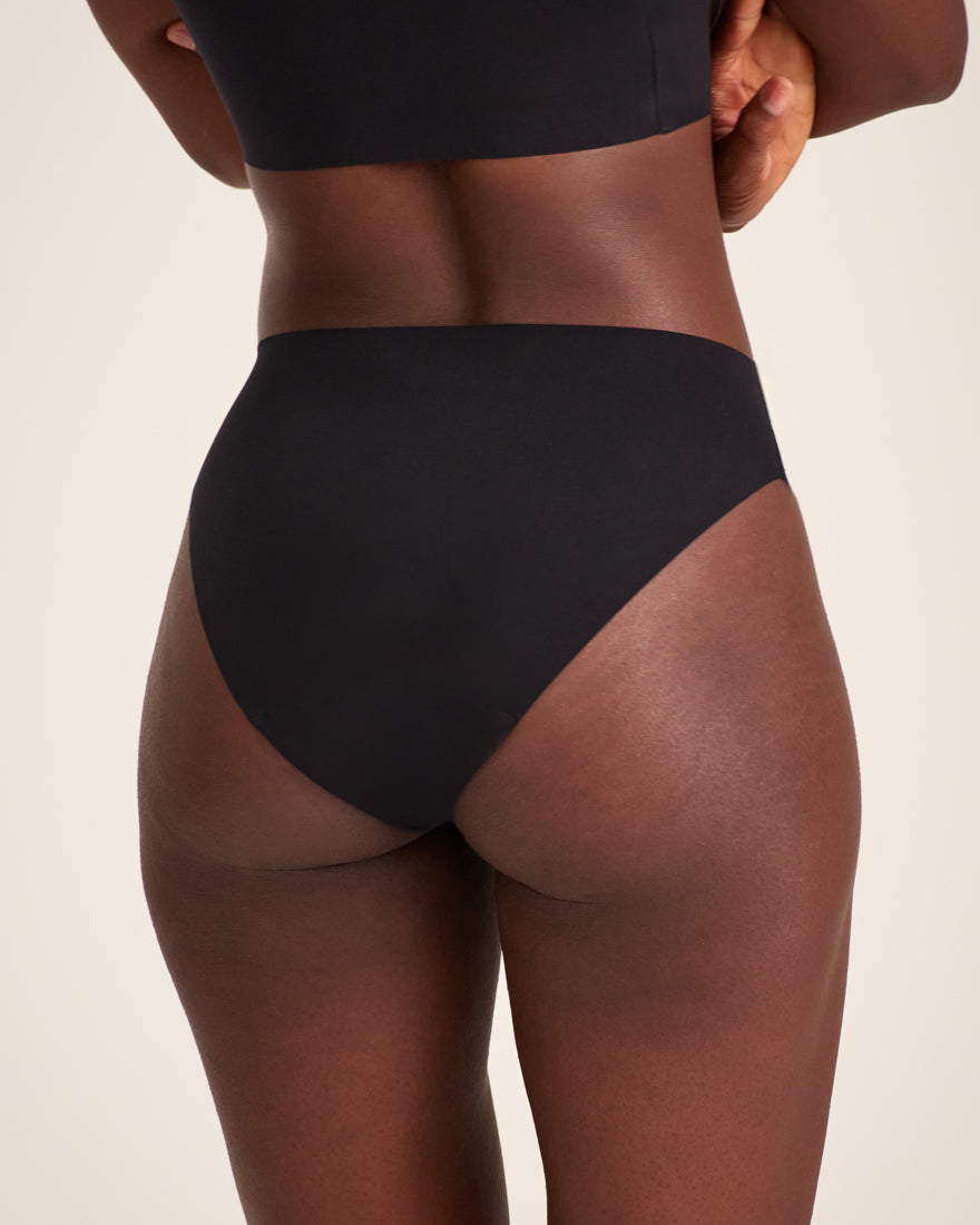 Modell trägt ooia Slip Seamless in Schwarz – nahtlose Periodenunterwäsche im klassischen Schnitt. Rückansicht.