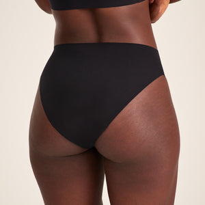 Modell trägt ooia Slip Seamless in Schwarz – nahtlose Periodenunterwäsche im klassischen Schnitt. Rückansicht.