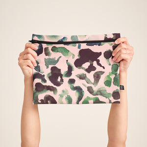 Modell hält die ooia Wetbag Maxi, in großem Design, mit rosa-grün-schwarzem Aufdruck und flüssigkeitsundurchlässigem Innenstoff.