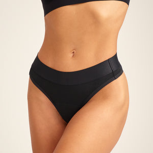 Modell trägt ooia Color Clash – Brazilian in Schwarz – Periodenunterwäsche mit breitem Bund.