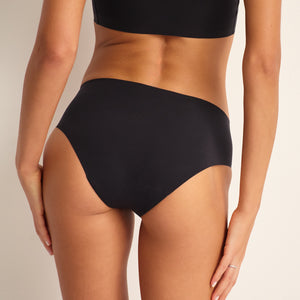 Modell trägt ooia Hipster Seamless in Schwarz – nahtlose Periodenunterwäsche. Rückansicht.