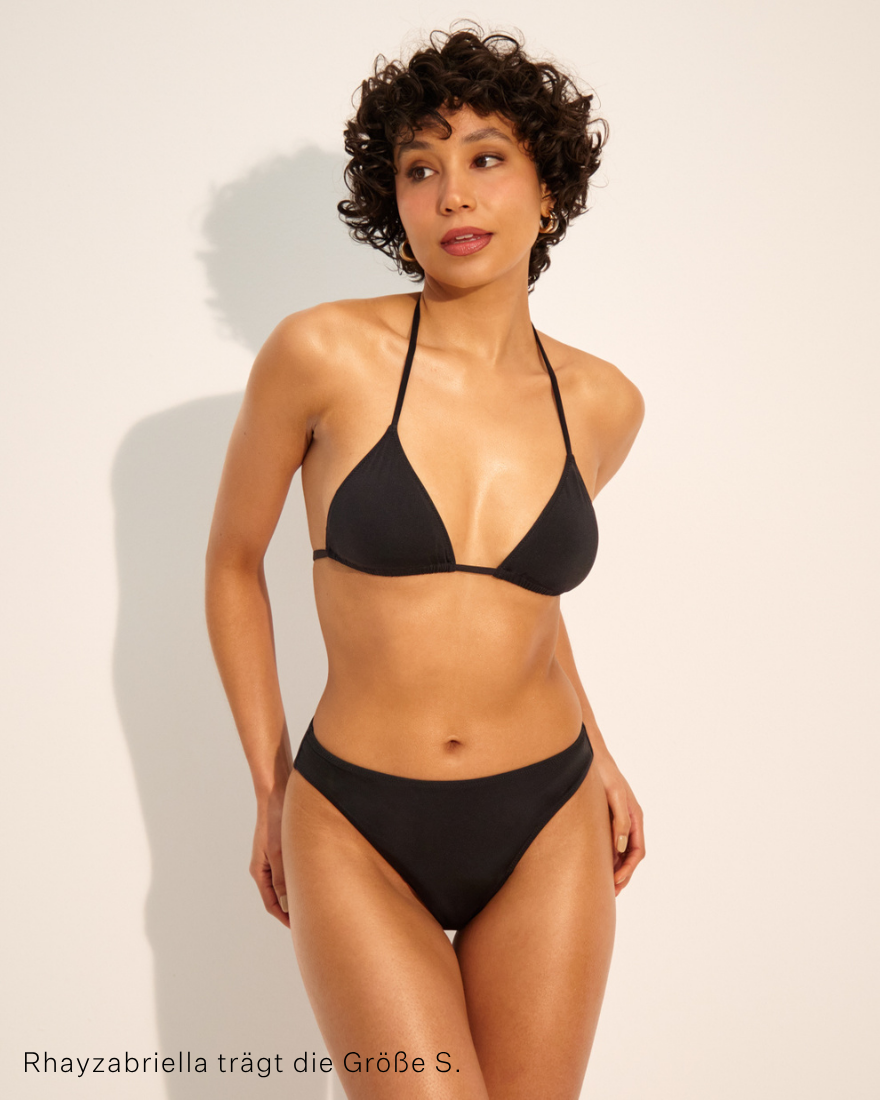 Das Modell trägt ooia Bademode Triangle Top in schwarz zum Binden im Hals und Rücken.
Frontal stehend