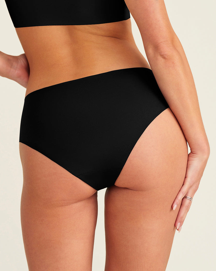 Modell trägt ooia everyday Hipster Seamless in Schwarz - nahtlose Unterwäsche die Slipeinlagen ersetzt. Rückansicht.