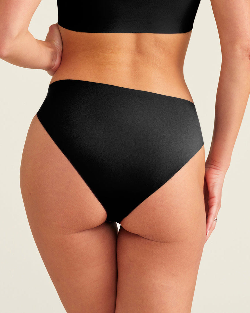 Modell trägt ooia everyday Slip Seamless in Schwarz – nahtlose Unterwäsche, die Slipeinlagen ersetzt. Rückansicht.