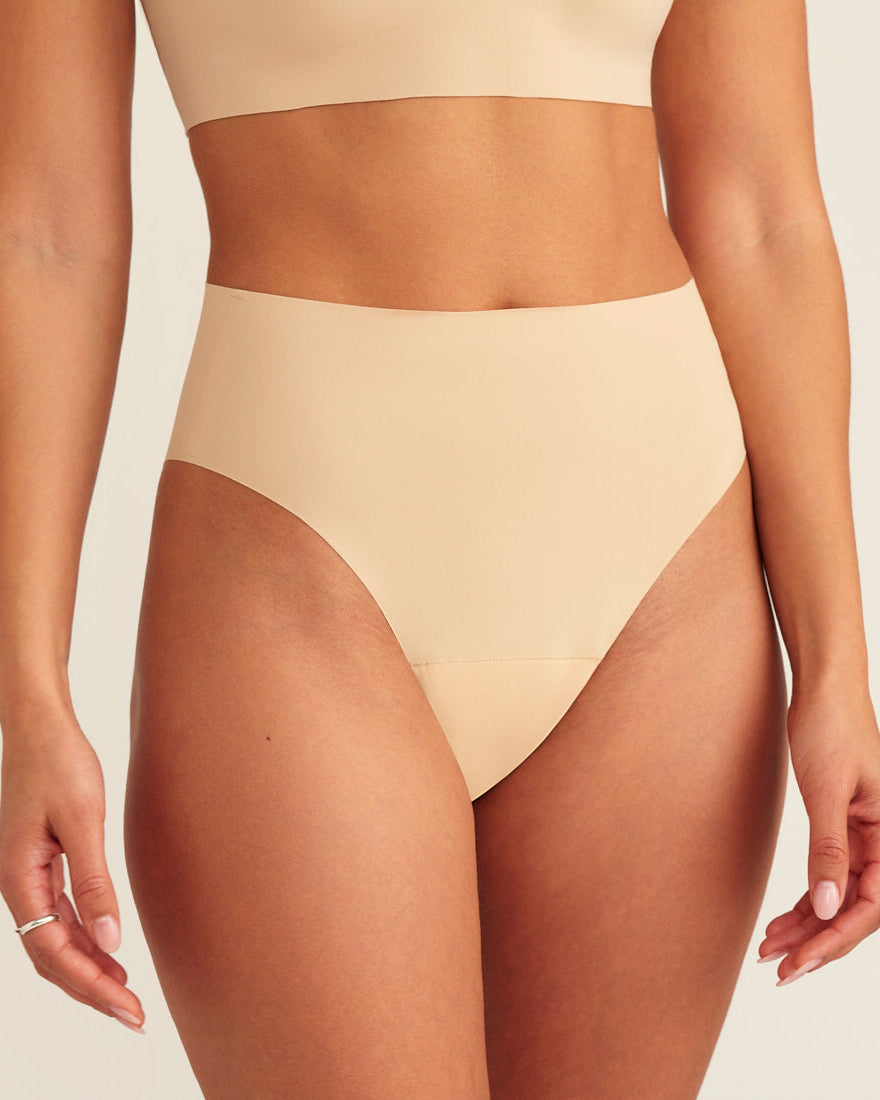 Modell trägt ooia Perioden Highwaist Seamless Cheeky in Beige – nahtloser Slip mit hoher Taille und Beinausschnitt