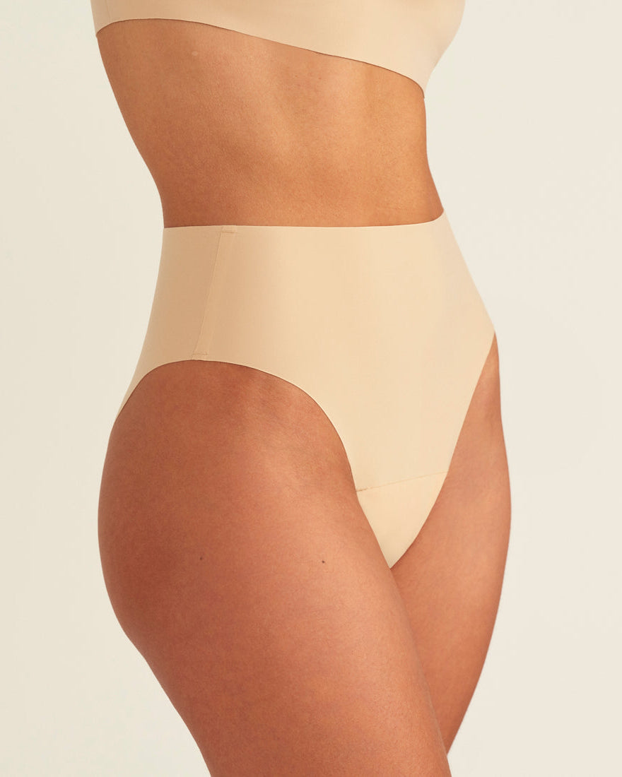 Modell trägt ooia Perioden Highwaist Seamless Cheeky in Beige – nahtloser Slip mit hoher Taille und Beinausschnitt