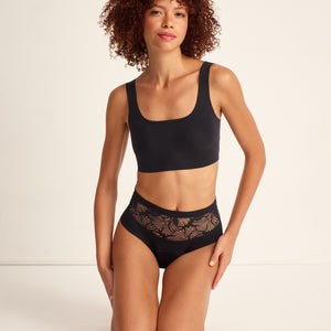 Modell trägt Periodenunterwäsche Highwaist Seamless Lace extra stark in schwarz mit nahtlosem Design mit breiter Spitze am Bund.
Frontal, kniend