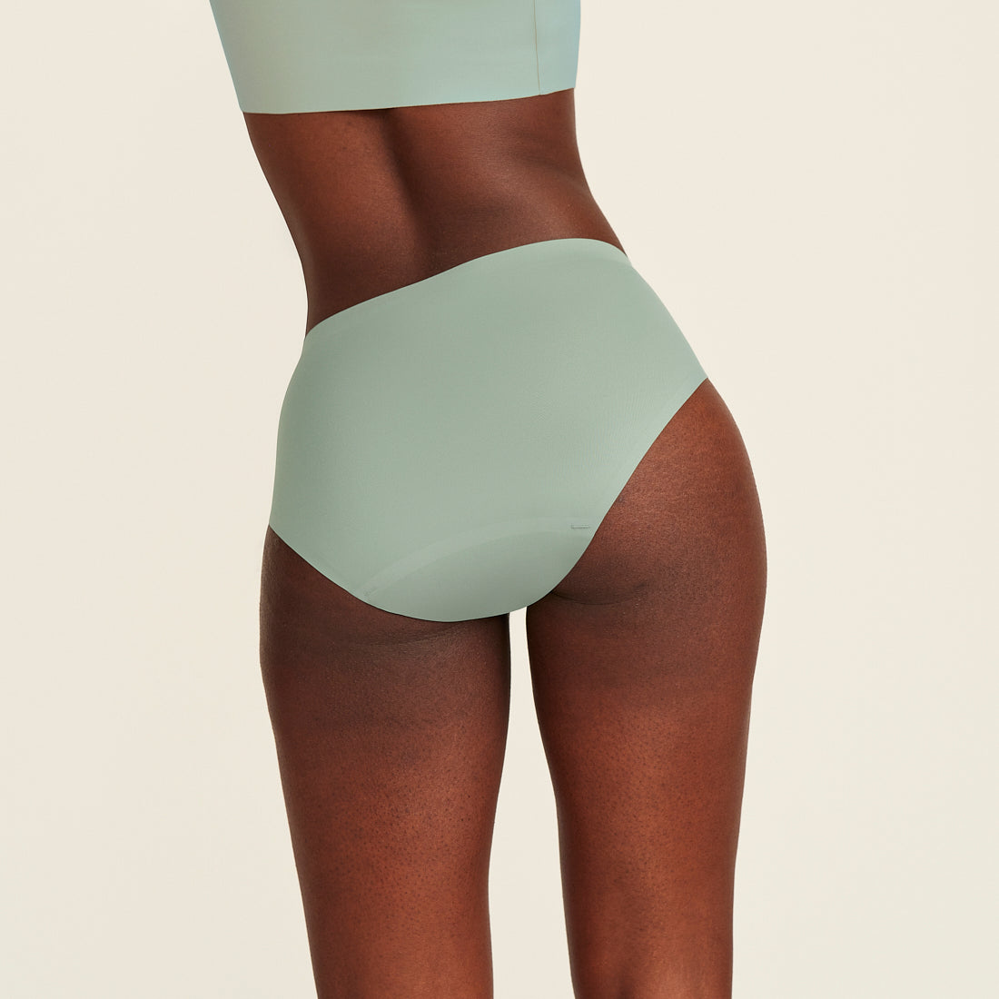 Modell trägt ooia Periodenunterwäsche Hipster Seamless in sage mit nahtlosem Design, Rückansicht