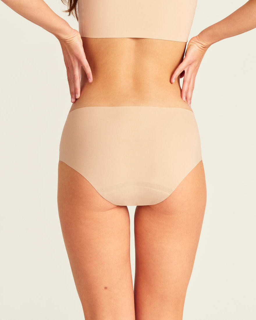 Modell trägt nahtlose ooia Periodenunterwäsche Hipster Seamless Extra Strong in beige. Rückansicht.