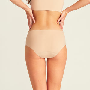 Modell trägt nahtlose ooia Periodenunterwäsche Hipster Seamless Extra Strong in beige. Rückansicht.