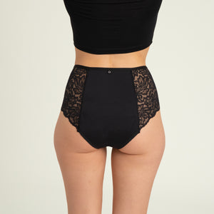 Modell trägt ooia Highwaist Lace Extra Strong in Schwarz – elegante Periodenunterwäsche mit hohem Spitzenbund und Spitzeneinsätzen. Rückansicht.