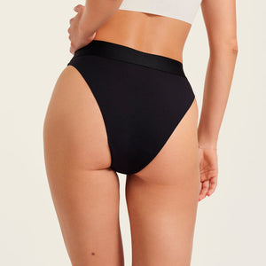 Modell trägt ooia Slip Seamless Cheeky in Schwarz – nahtlose Periodenunterwäsche mit hohem Beinausschnitt. Rückansicht.