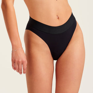 Modell trägt ooia Slip Seamless Cheeky in Schwarz – nahtlose Periodenunterwäsche mit hohem Beinausschnitt