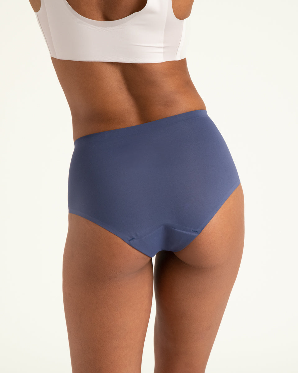 Modell trägt ooia Highwaist Seamless in Smoky Blue – nahtlose Periodenunterwäsche mit hohem Bund. Rückansicht.