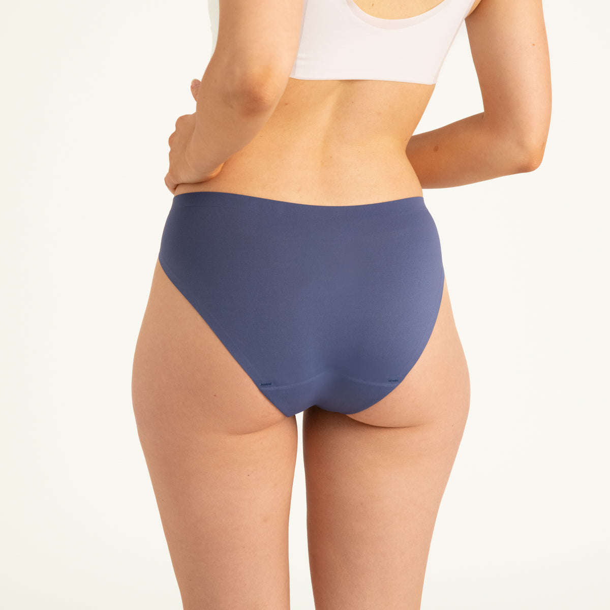 Modell trägt ooia Slip Seamless in Smoky Blue – nahtlose Periodenunterwäsche im klassischen Schnitt. Rückansicht.