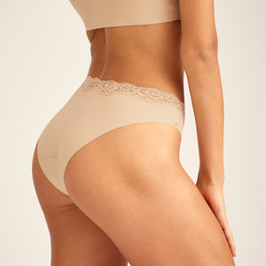 Modell trägt ooia Periodenunterwäsche Slip Seamless Lace Extra Strong in Beige