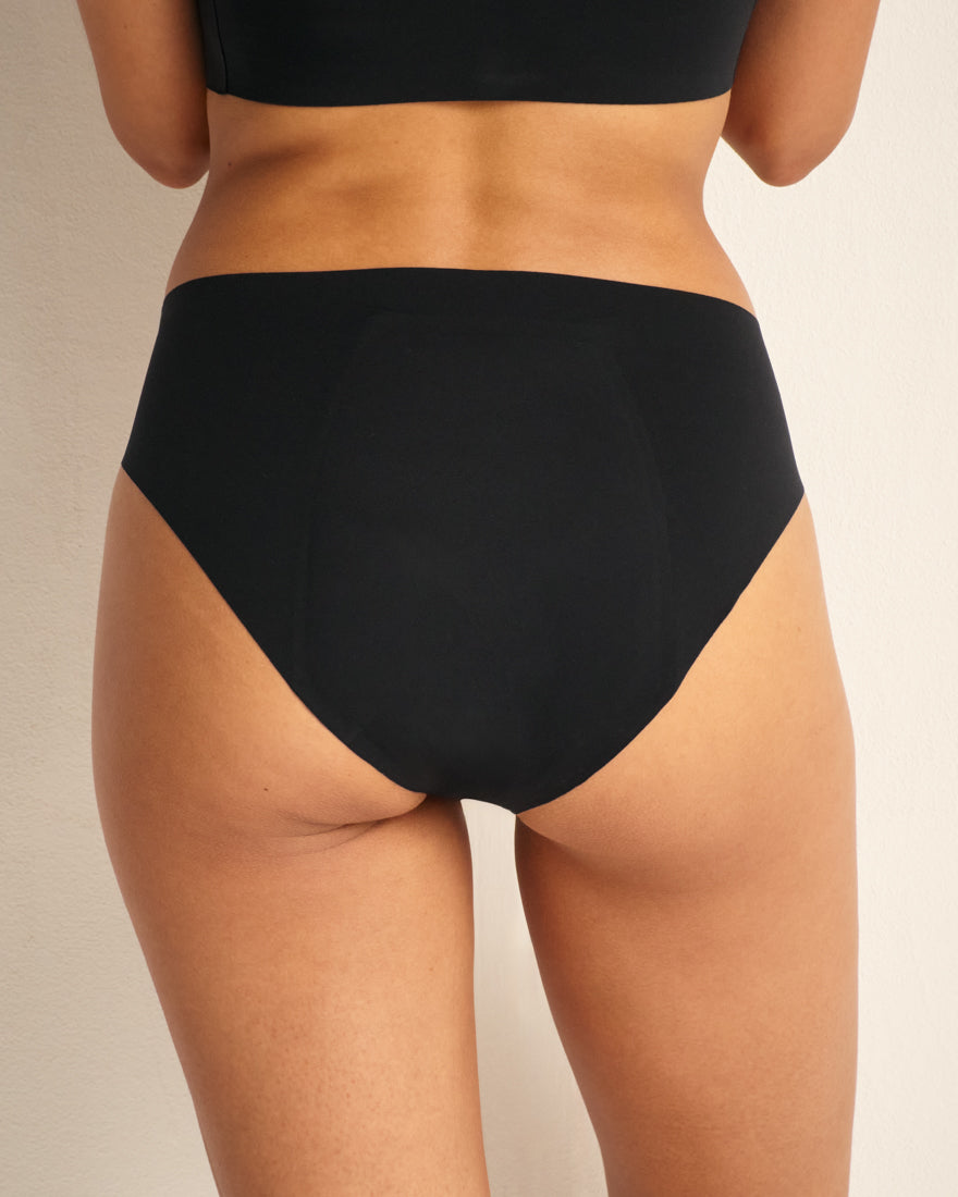 Modell trägt Periodenunterwäsche Slip Seamless Ultimate in schwarz mit nahtlosem Design.
von hinten