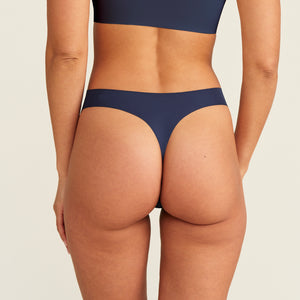 Modell trägt den ooia Periodenunterwäsche String Seamless in midnight mit leichter Saugstärke, Rückansicht