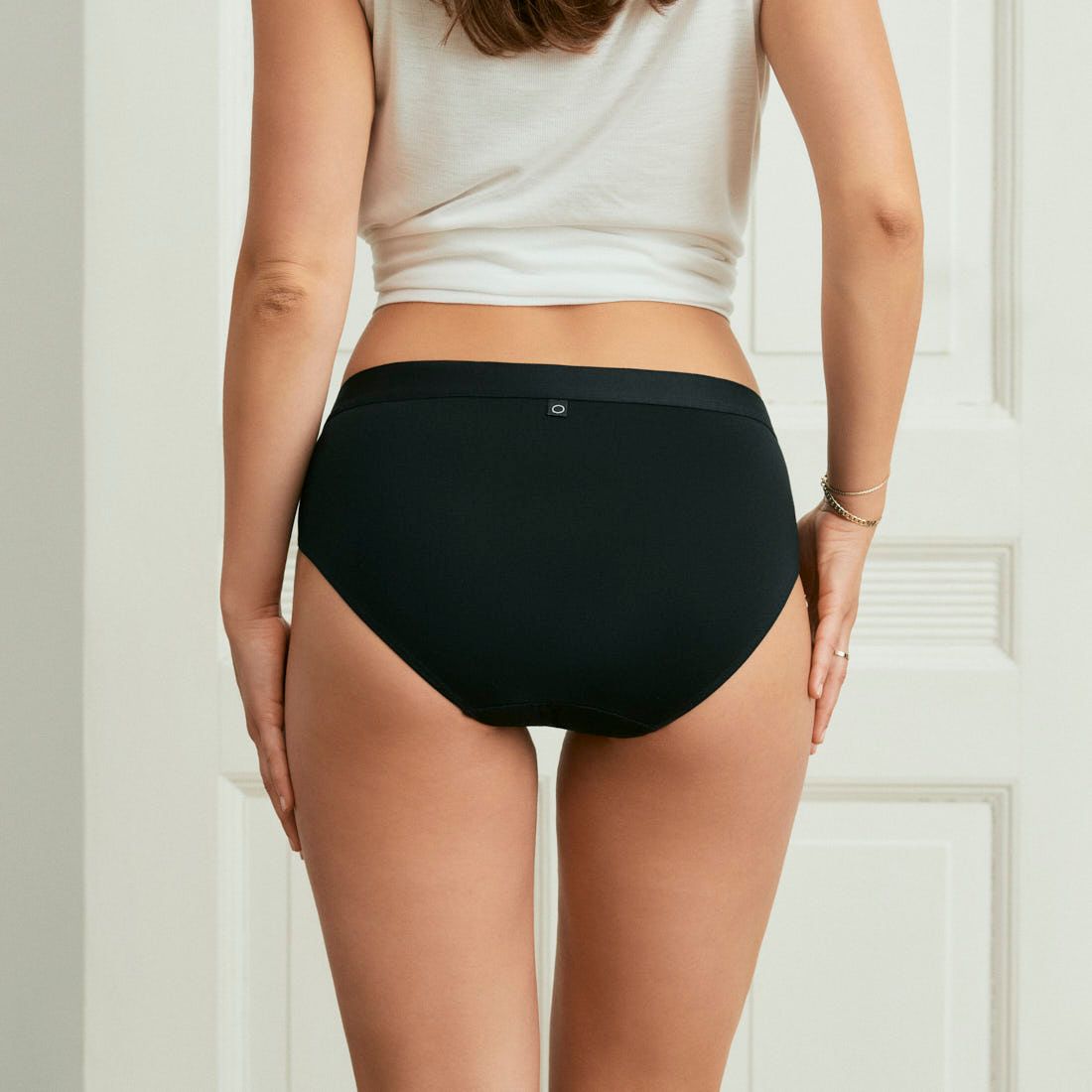 Modell trägt ooia everyday Hipster in Schwarz – Unterwäsche mit breitem Bund, die Slipeinlagen ersetzt. Rückansicht.