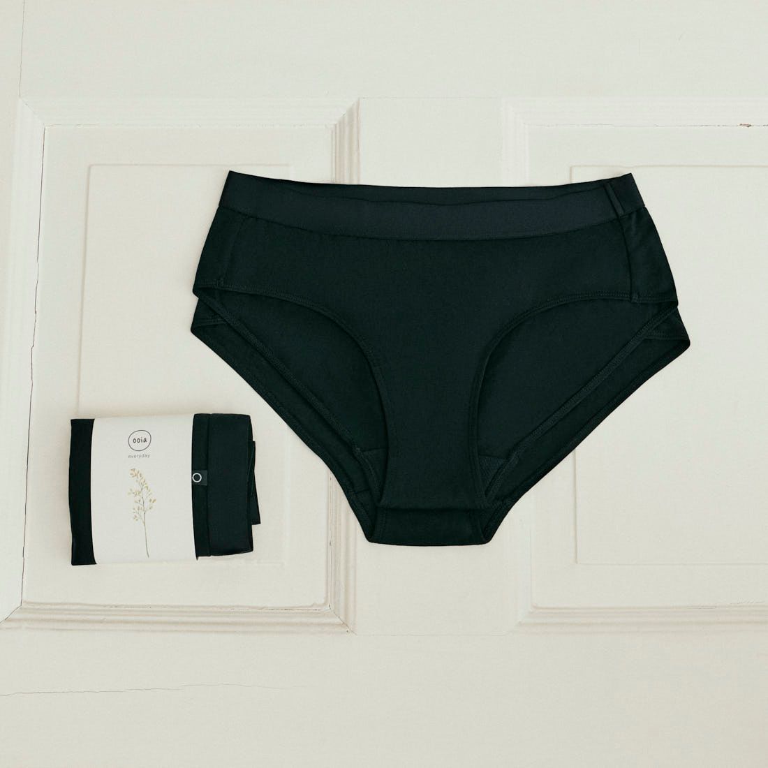 2 Stück ooia everyday Hipster in Schwarz – Unterwäsche mit breitem Bund, die Slipeinlagen ersetzt, liegen auf hellem Untergrund.