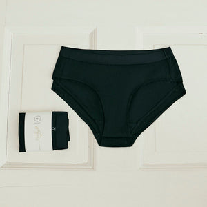 2 Stück ooia everyday Hipster in Schwarz – Unterwäsche mit breitem Bund, die Slipeinlagen ersetzt, liegen auf hellem Untergrund.