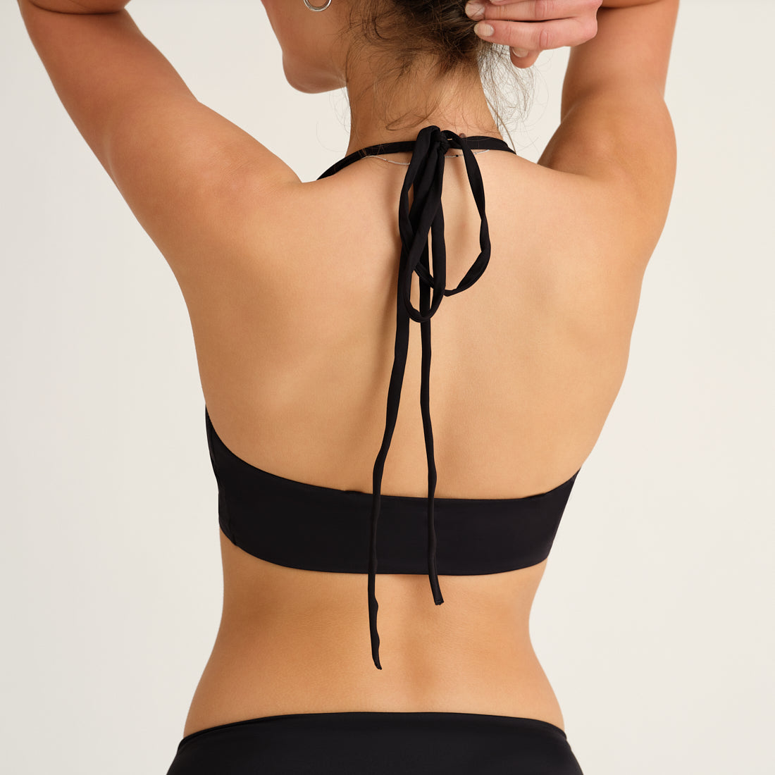 Modell trägt das ooia Beach Triangle Top in Schwarz – Bikini-Oberteil mit verstellbaren Trägern im klassischen Triangel-Design. Rückansicht.