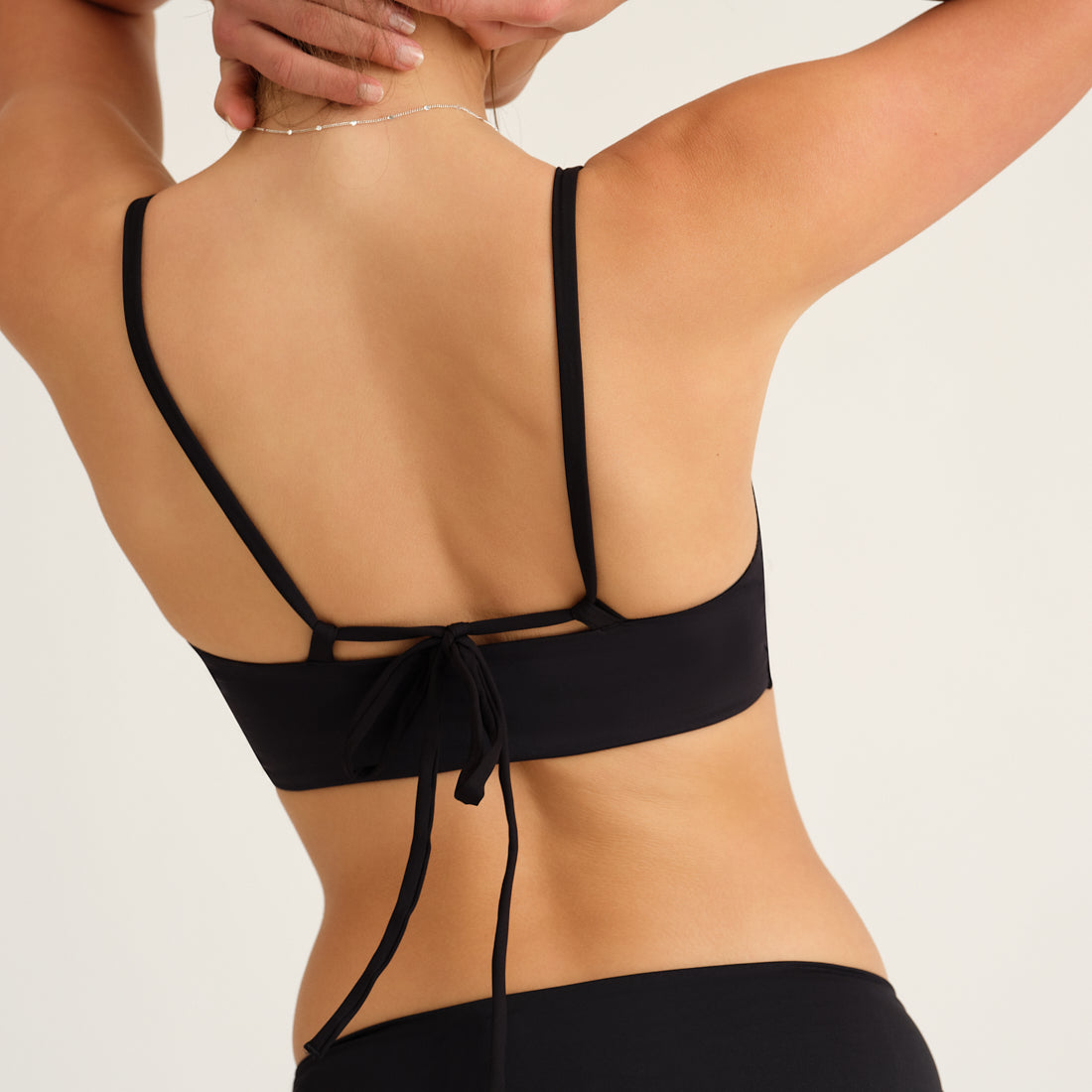 Modell trägt das ooia Beach Triangle Top in Schwarz – Bikini-Oberteil mit verstellbaren Trägern im klassischen Triangel-Design. Rückansicht.