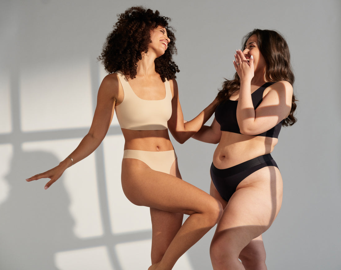 zwei Frauen in beiger und schwarzer nahtloser Periodenunterwäsche lachen