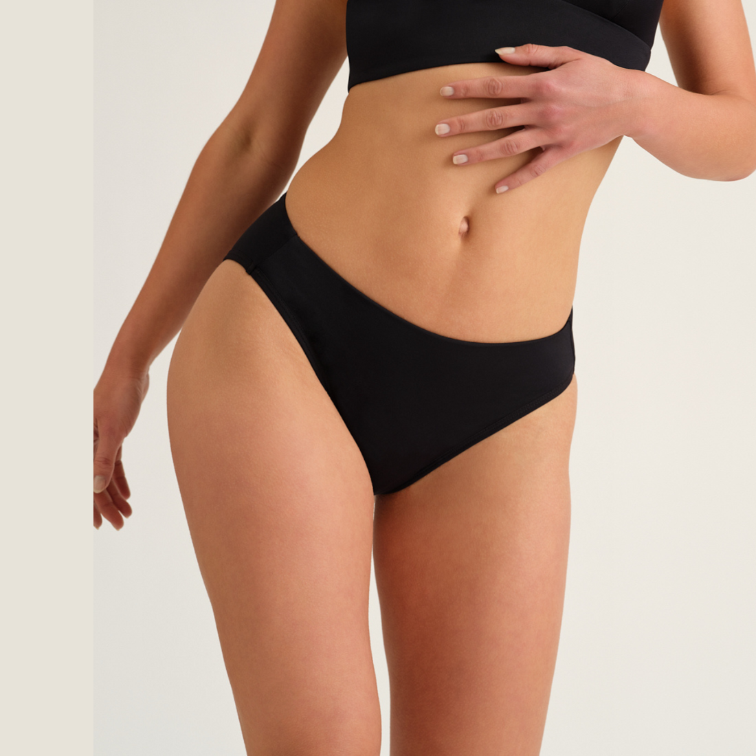 Modell trägt den ooia Beach Slip in Schwarz - Periodenbikini-Slip im klassischen Design
