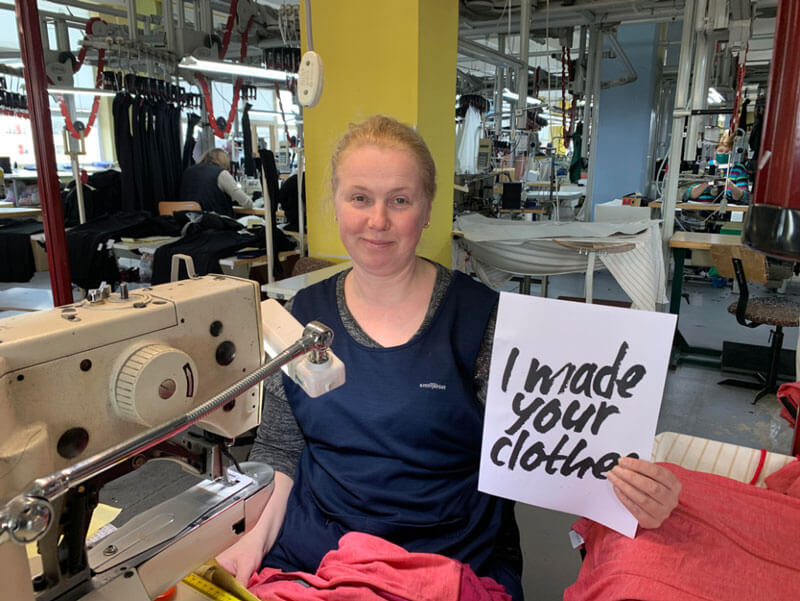 eine Näherin in der Produktionsstätte hält ein Papier mit der Aufschrift I made your ooias
