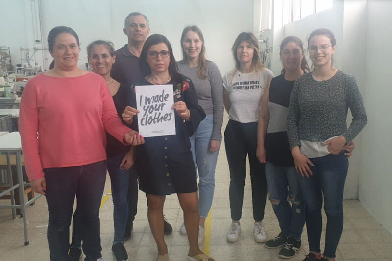 NäherInnen in einer ooia Produktionsstätte halten ein Papier mit der Aufschrift I made your clothes 