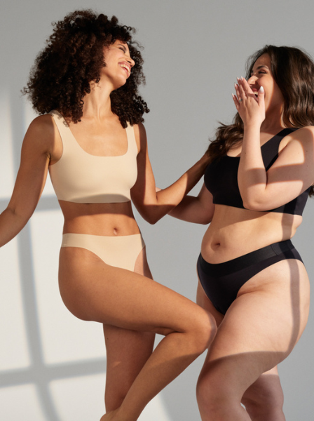 Zwei Models posieren lachend zusammen in schwarzer und beiger nahtloser Periodenunterwäsche