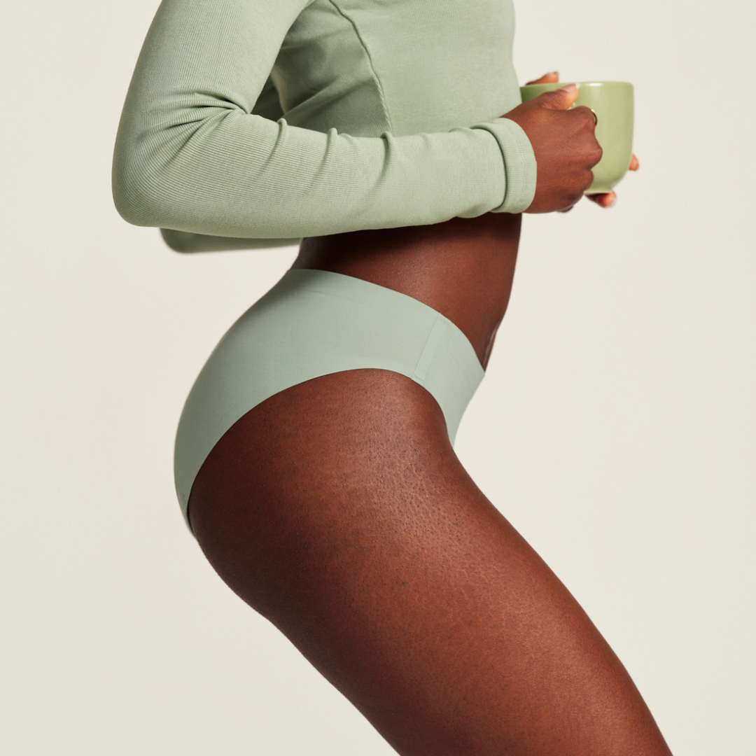 Bildausschnitt eines Models in nahtloser sage Periodenunterwäsche mit einer Tasse Tee in der Hand